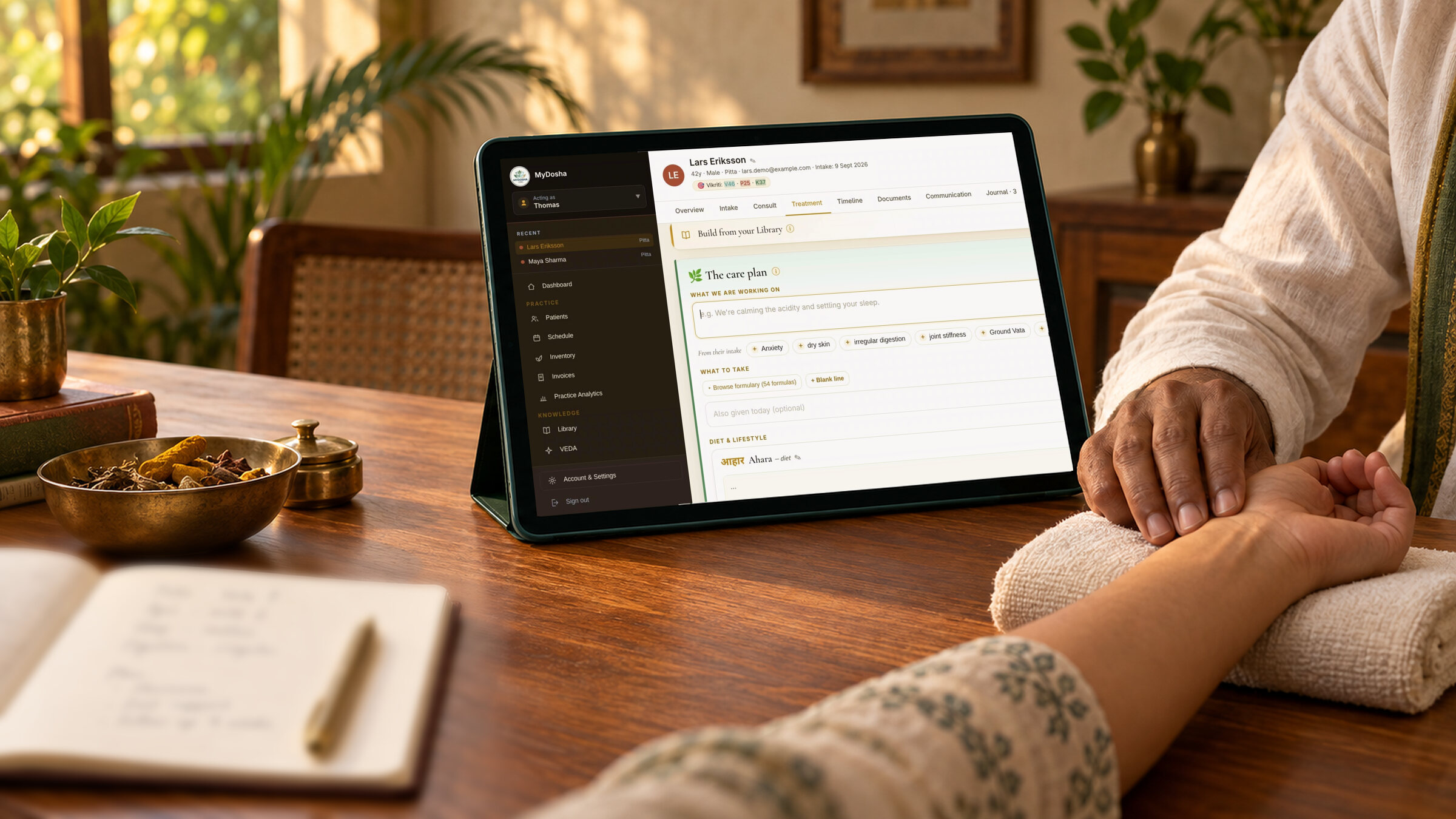 Ayurvedischer Behandler tastet den Puls eines Patienten, daneben ein Tablet mit einem MyDosha-Behandlungsplan